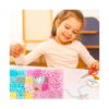 Set DIY de bijuterii cu unicorn, fetiță la masă care înșiră mărgele, cu organizatorul plin de mărgele pastel
