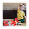 set-senzorial-aventura-dino-5-in-1-utilizare-2 Set senzorial Aventură Dino 5 în 1, copil mic în tricou galben, așezat pe pat, cu dinozaurul de pluș roșu în față