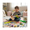 Set senzorial Primăvara, băiat pe covor ținând puișorul squishy în costum de broscuță și o placă tangram din lemn; în jur tub