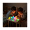 set-squishies-luminoase-jucarii-antistres-utilizare Set squishies luminoase, doi copii într-o cameră întunecată, la o măsuță, privind mai multe figurine squishy care strălucesc