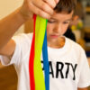 Șnur extensibil Fidget, prim-plan cu mâinile unui băiat care întind trei șnururi Fidget, verde, roșu și albastru