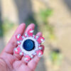 Spinner Fidget Among Us, o mână ține în palmă un spinner Among Us cu personaje roz și alb și cu centru albastru, în exterior