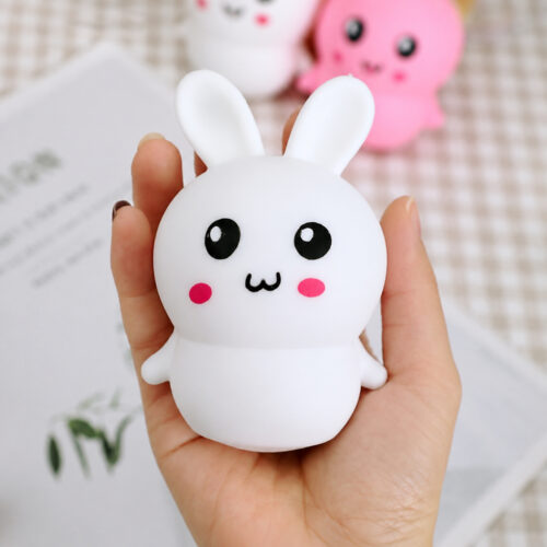 squishy-iepuras-alb Squishy iepuraș alb, mână care ține un squishy iepuraș alb cu obraji roz, pe fundal cu alte squishy-uri