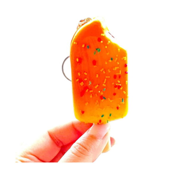 Squishy înghețată Bucuria copiilor, squishy portocalie ținută între degete, cu inelul de chei vizibil în spate