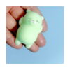 squishy-pisicuta-alb-7 Squishy pisicuță, verde deschis, strânsă în mână, pe fundal albastru
